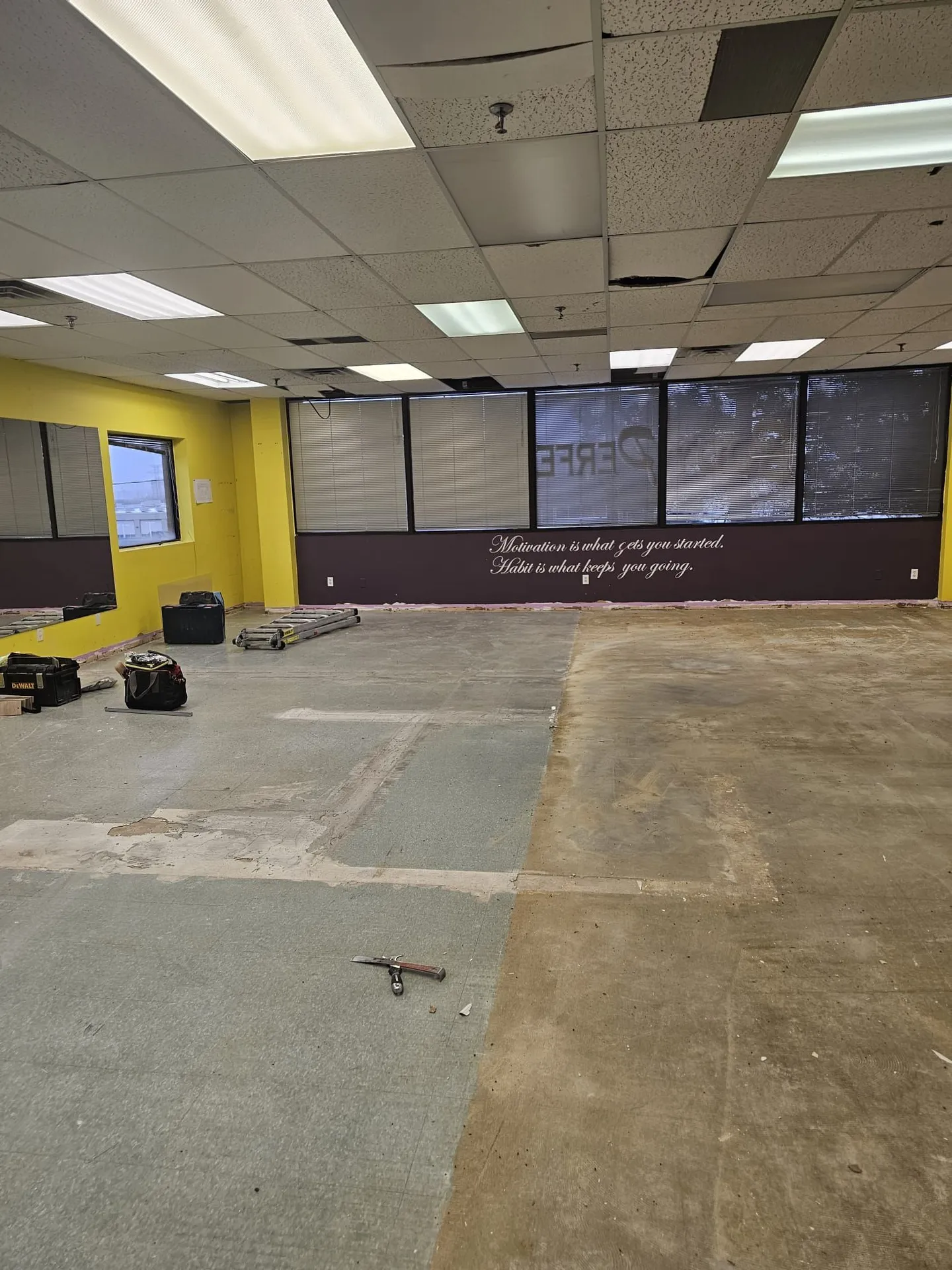 Interior demolition underway with carpet half-removed to the mastic and tools staged