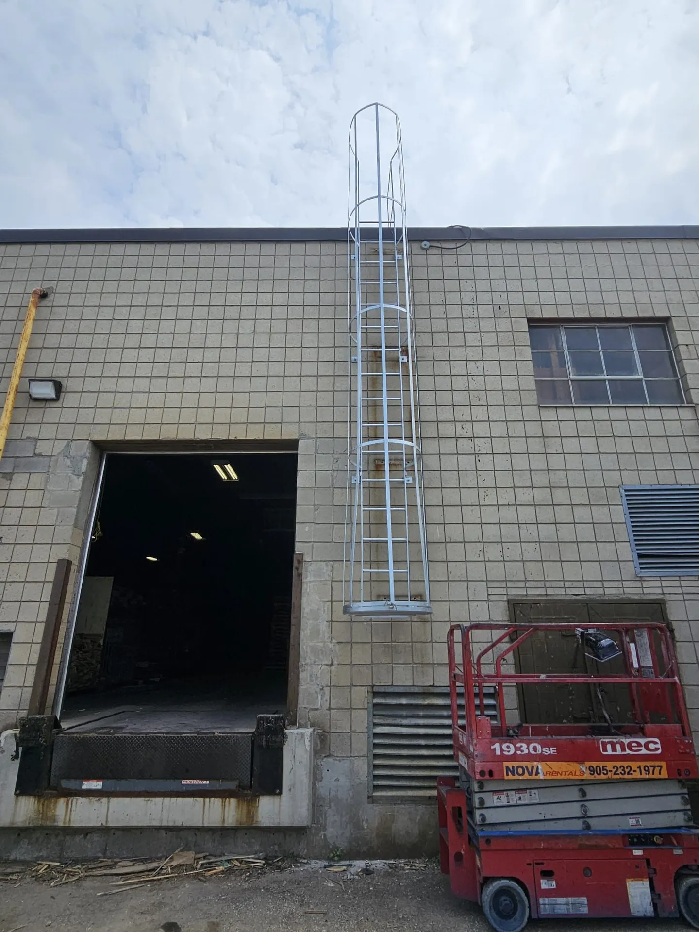New galvanized caged roof-access ladder installed beside an open dock door