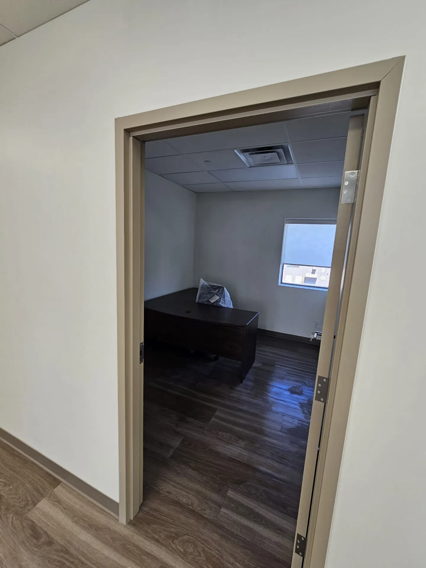 Private office glimpsed through a new doorway with dark wood desk and LVP flooring