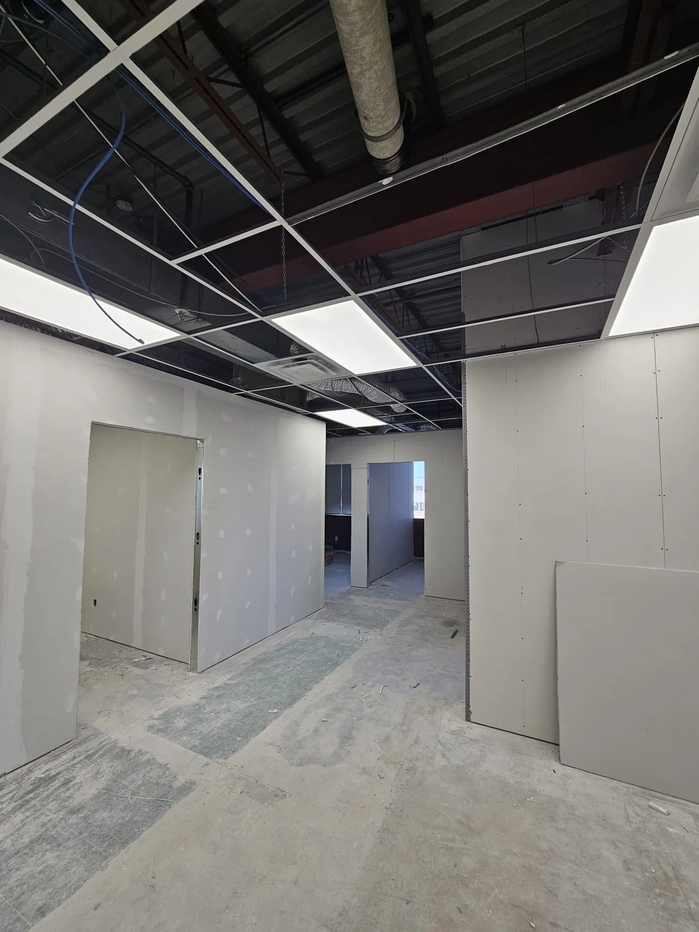 New LED panels in an open ceiling grid above freshly hung drywall partitions