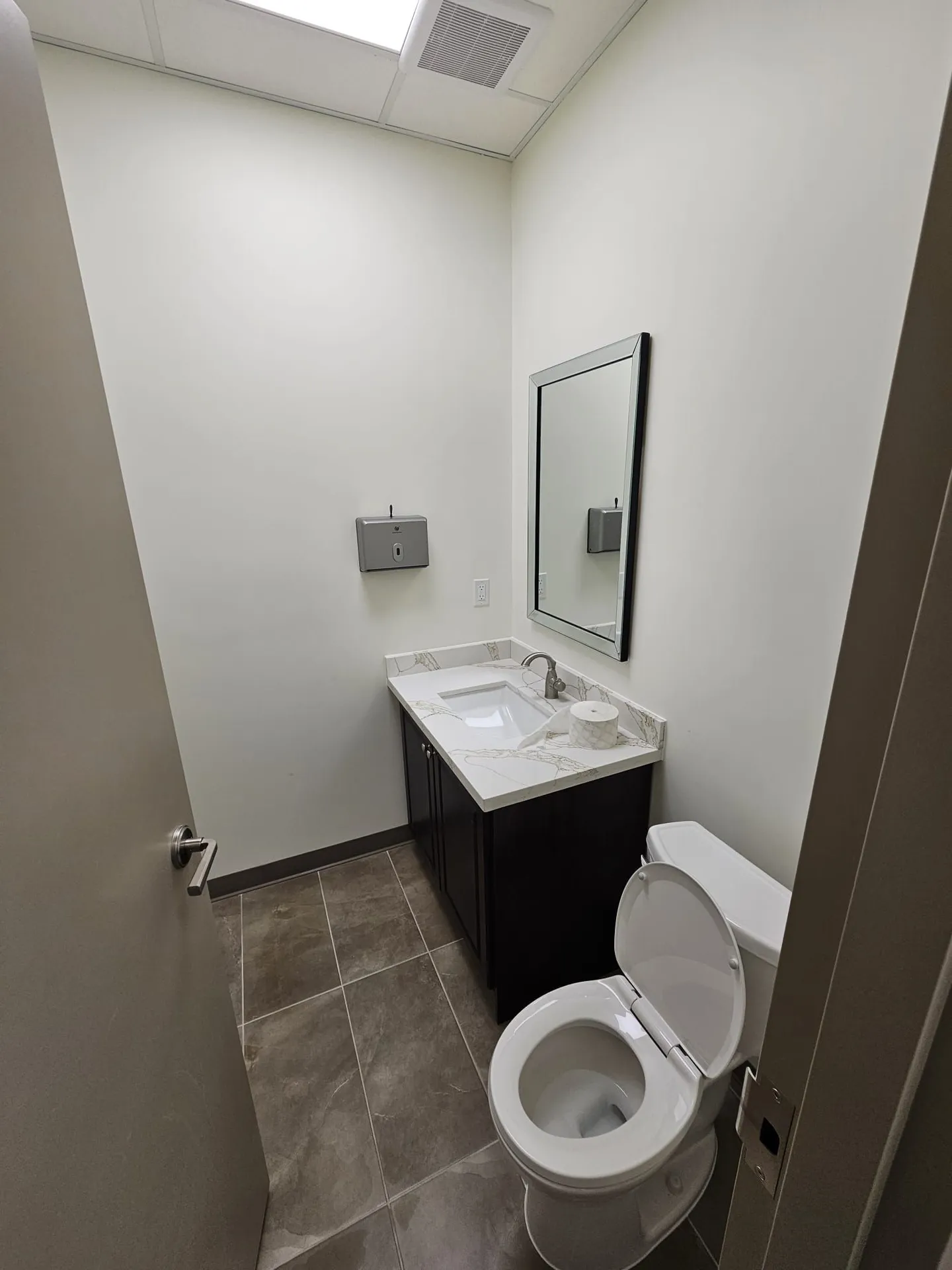 Finished washroom from a second angle with dark vanity, quartz top, mirror, and grey tile