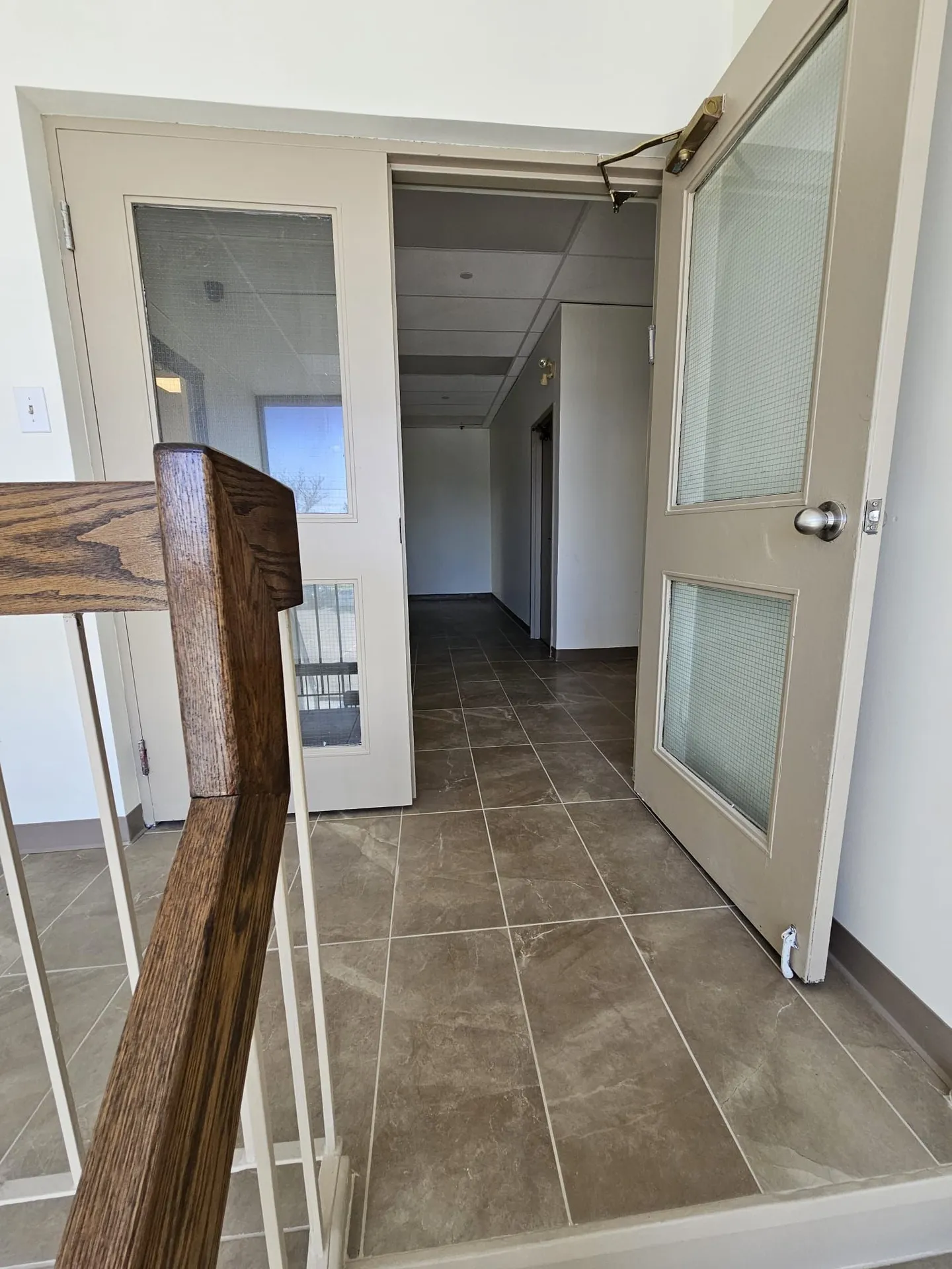 New suite entry double doors with frosted glazing seen from a stair landing with new tile and wood rail