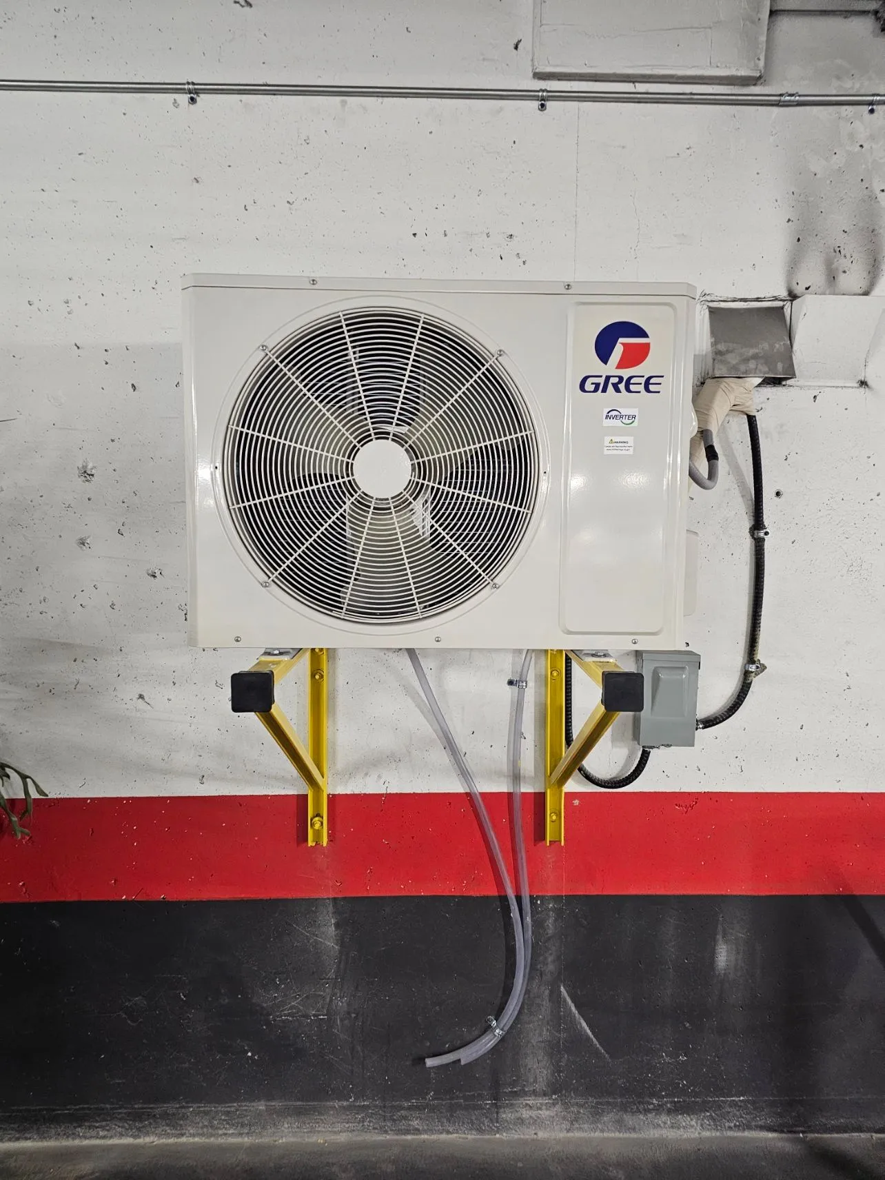 Condenser unit mounted on custom yellow steel brackets on a parkade wall