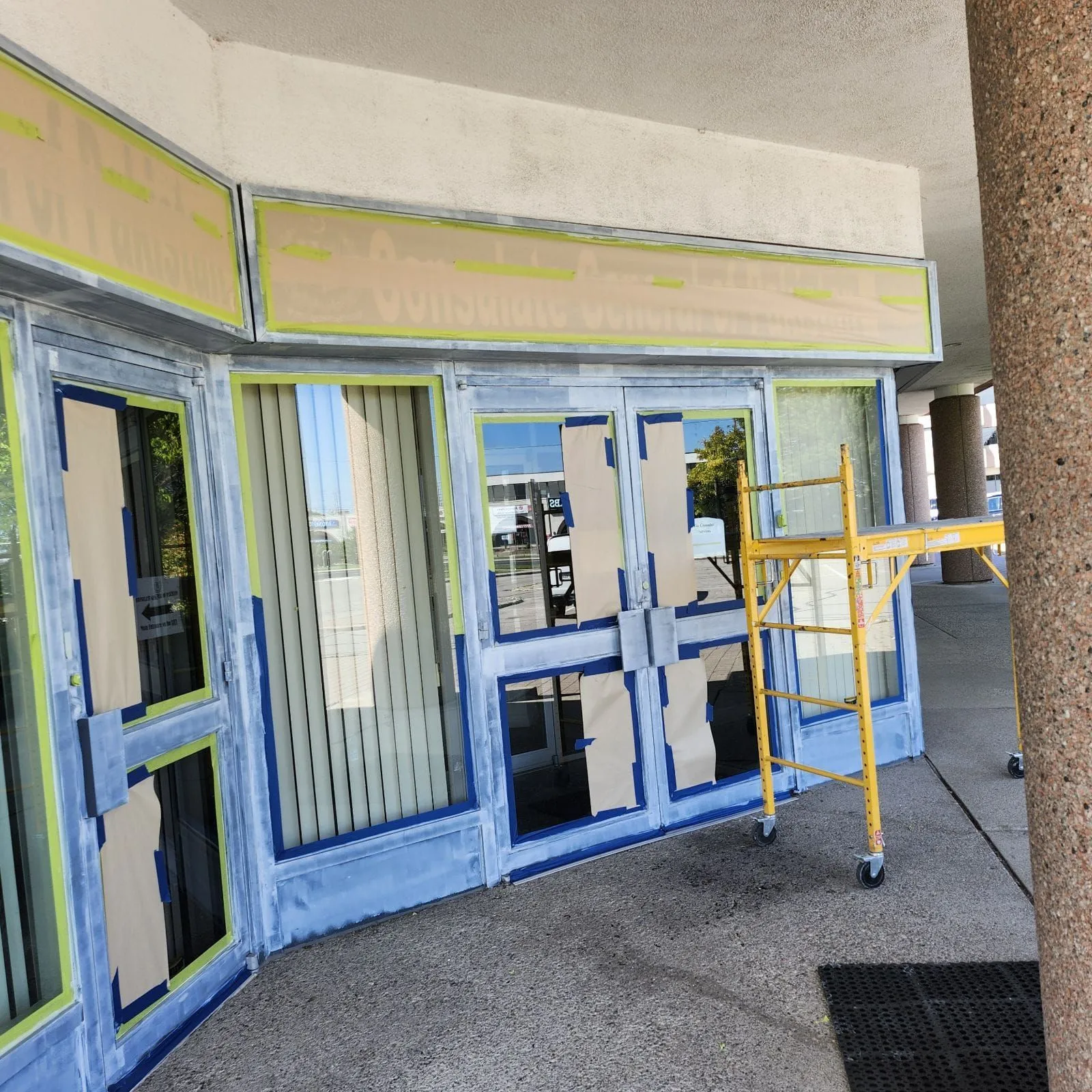Entrance doors masked for repaint with a yellow baker scaffold in place