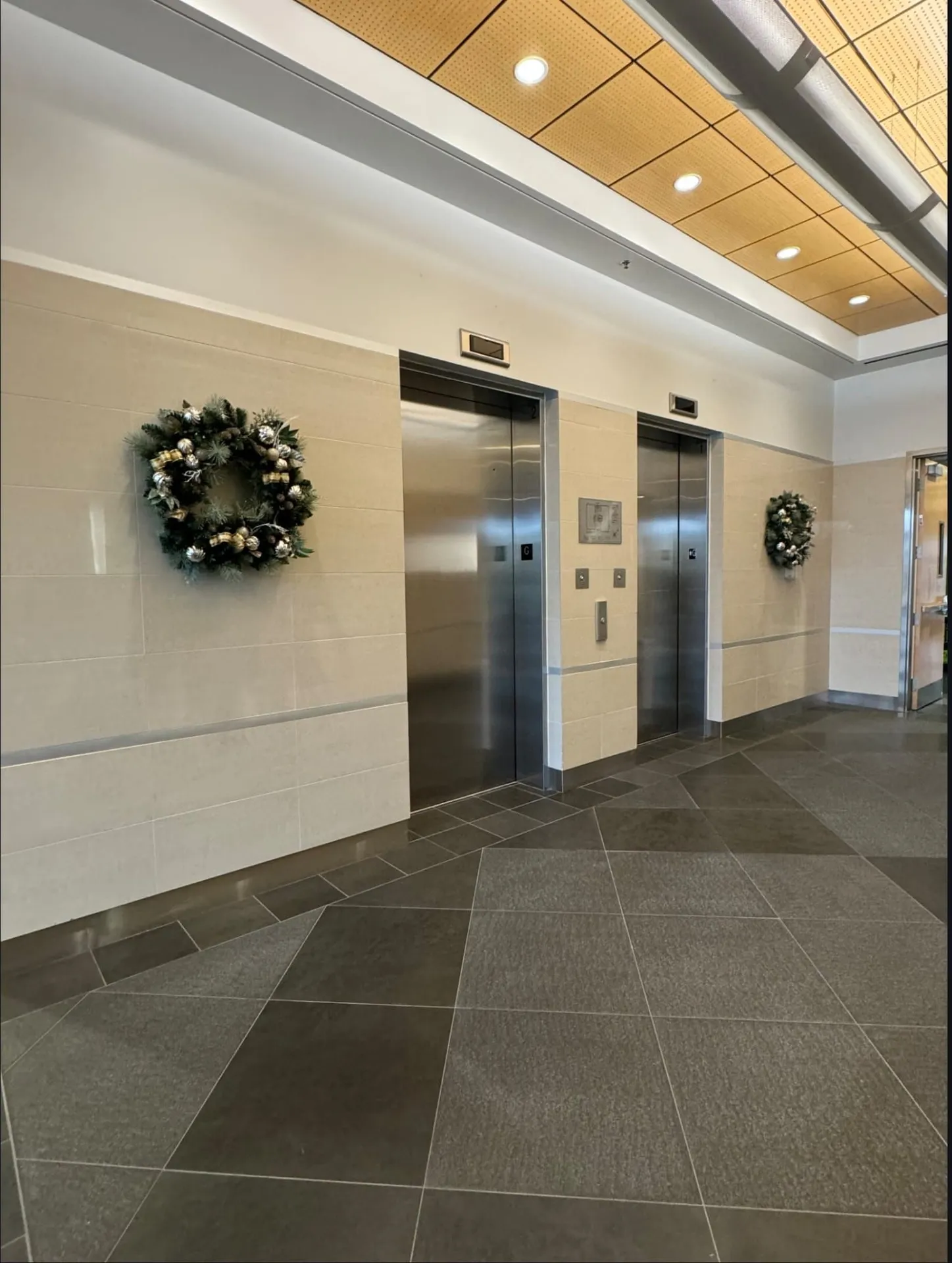 Elevator lobby with two large gold and silver wreaths on stone-tile walls