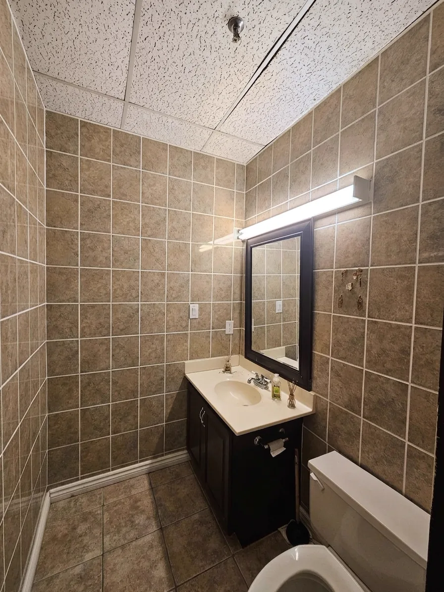 Washroom before: dated beige wall tile and worn vanity